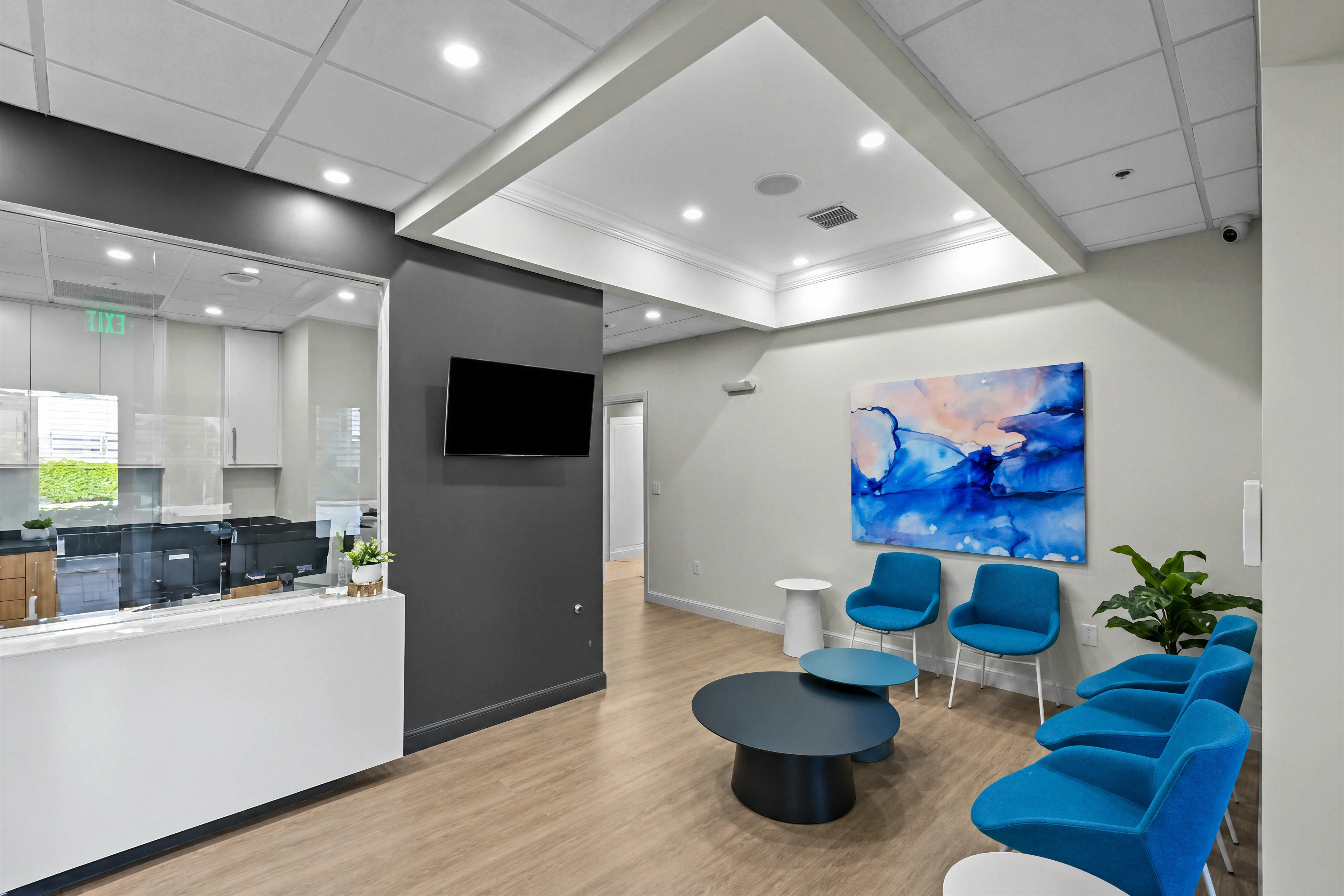 Medical office reception with blue chairs and glass partitions.