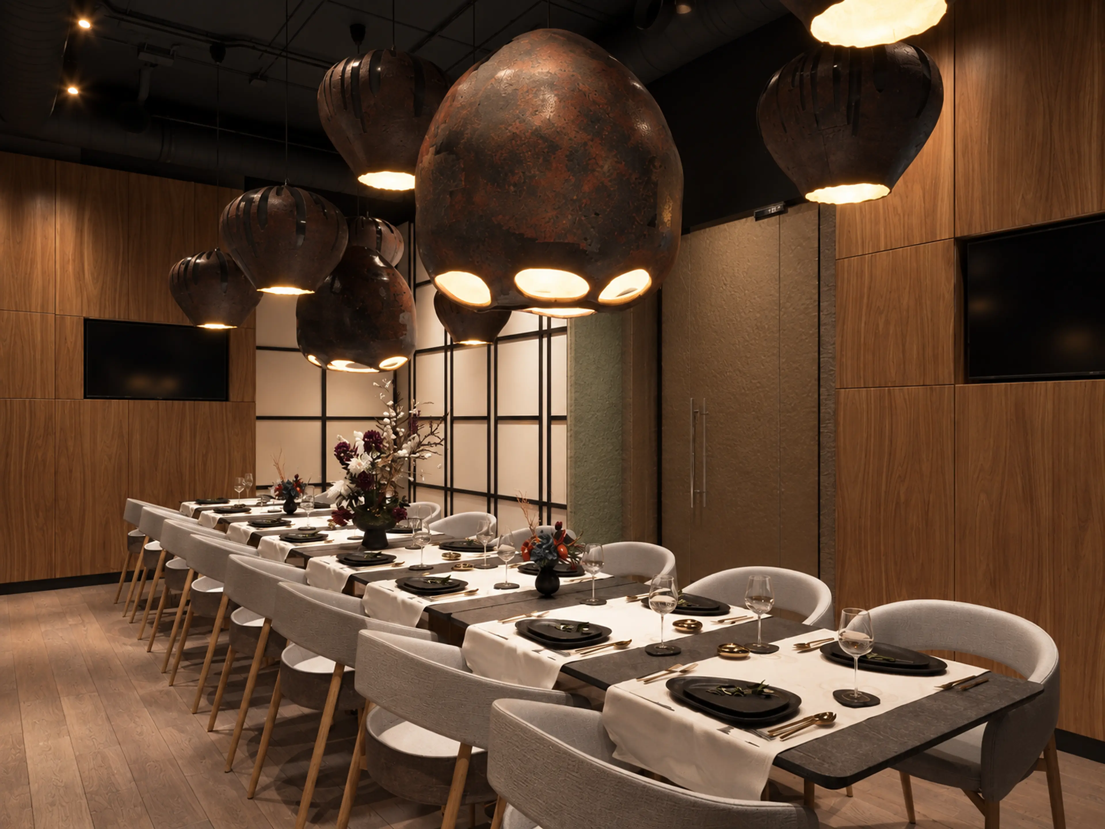 Photographic private dining room with a long set table and dark sculptural pendants.