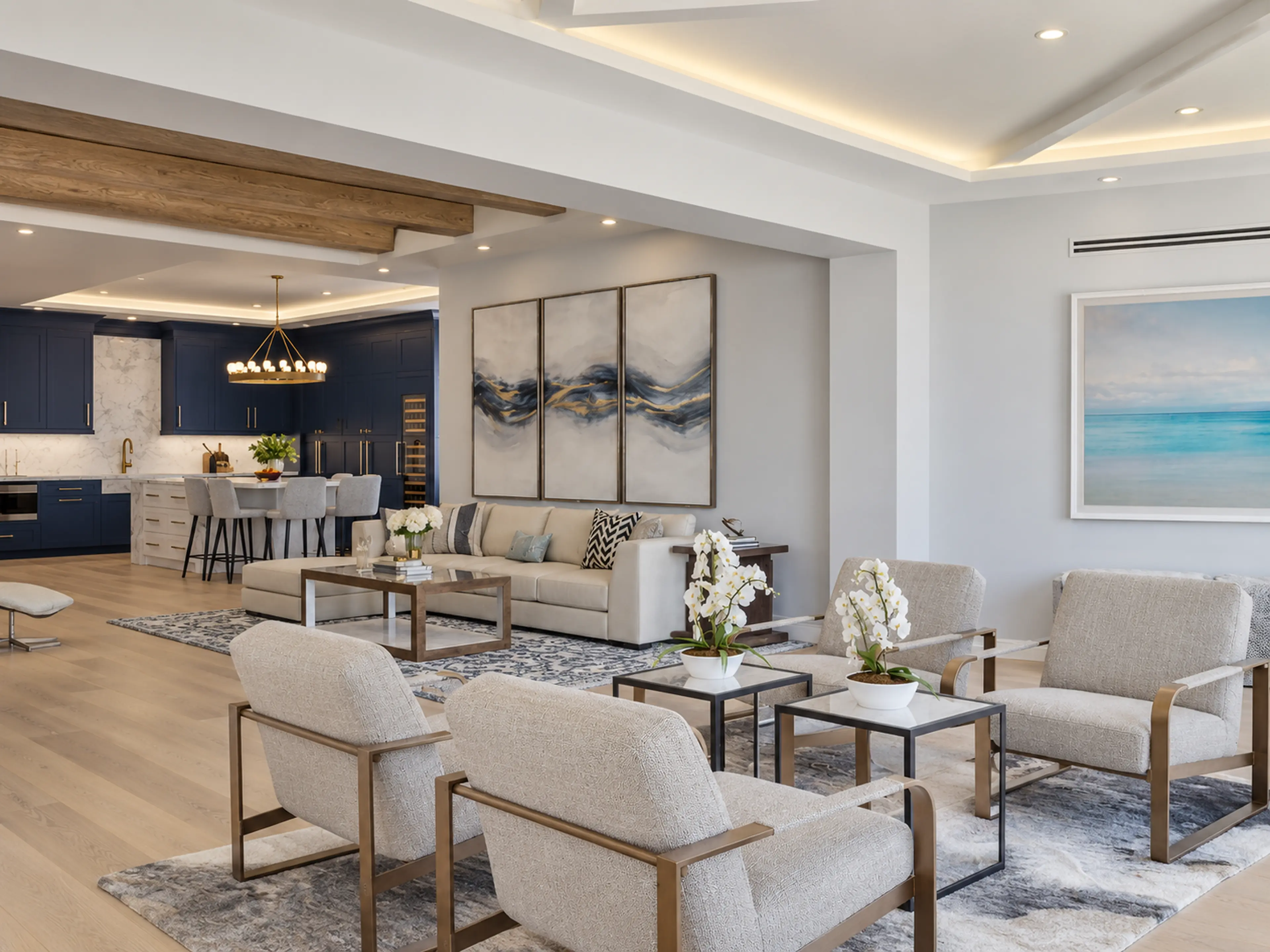 Photographic open living room with ocean-facing windows and a navy kitchen beyond.